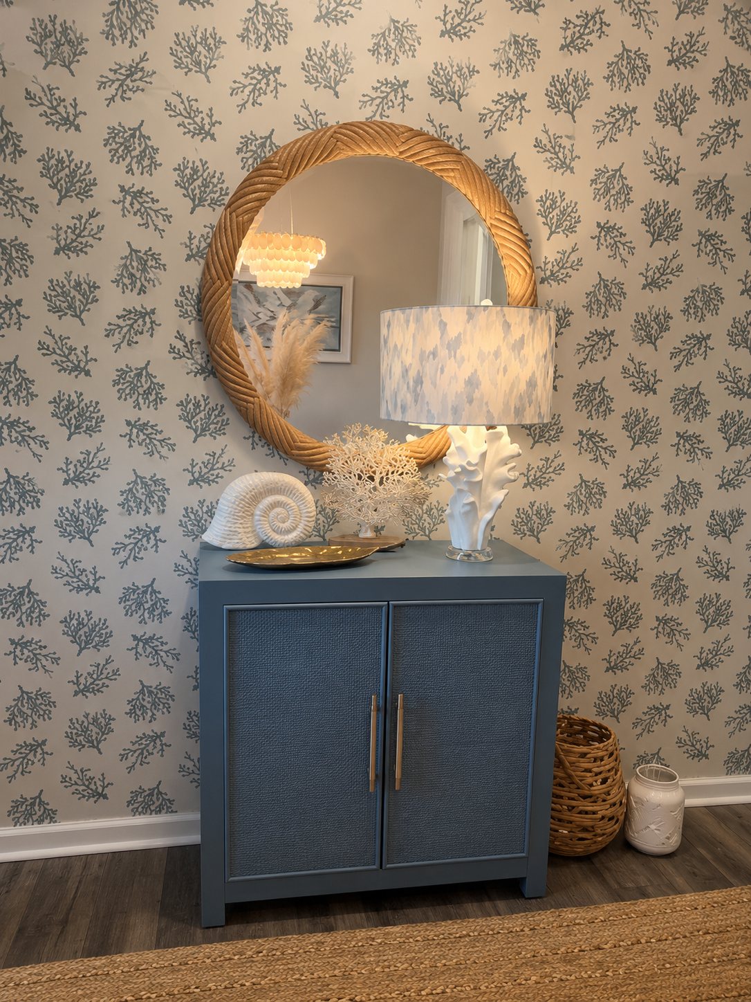 Coral-print wallpaper with a rope mirror over a blue cabinet